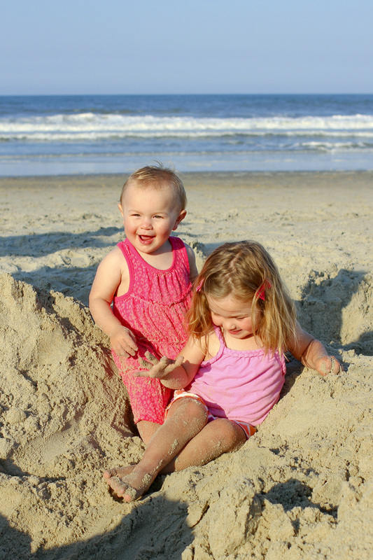 Two tiny sisters playing in the sand at the beach. By Calm Cradle Photo & Design