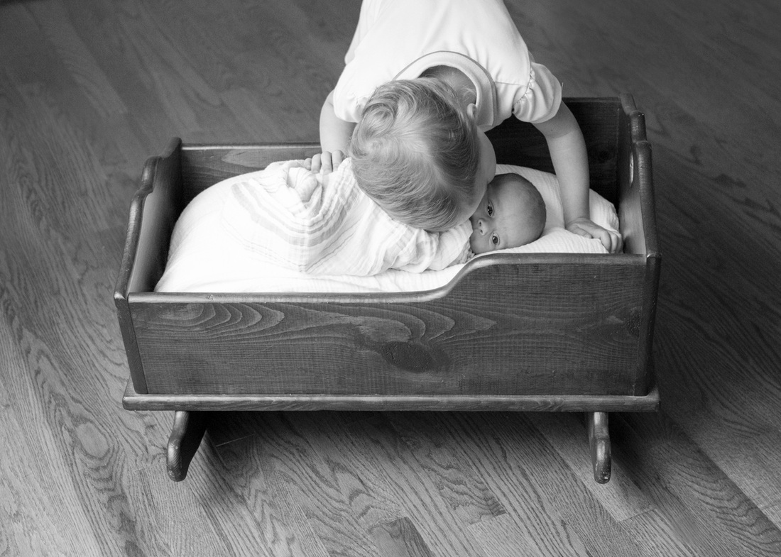 Newborn portraits: A kiss from her big sister. Lying in her grandmother's cradle in their new, empty house. Photography by Calm Cradle Photo & Design
