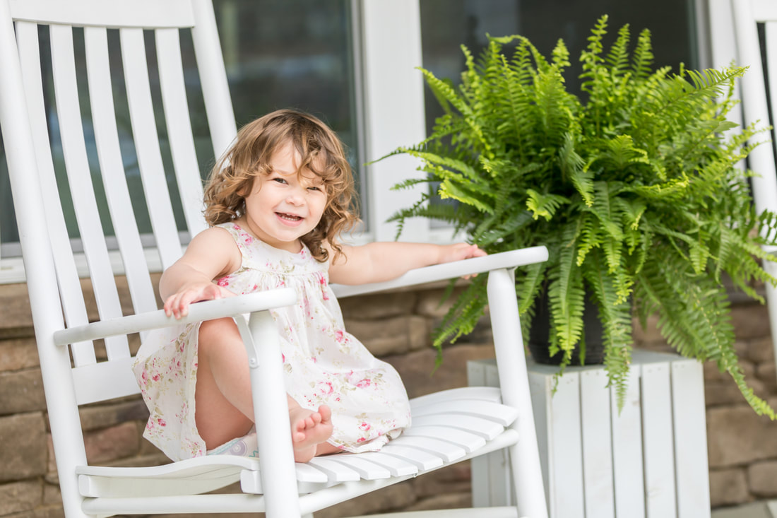 Lifestyle portraits: 2-year-old girl on the front porch with flowers and ferns. By Calm Cradle Photo & Design (Chapel Hill, North Carolina, NC)
