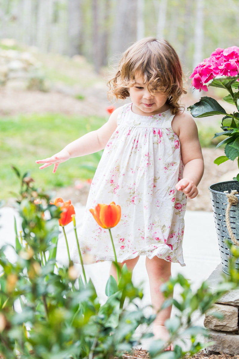 Lifestyle portraits: 2-year-old girl on the front porch with flowers and ferns. By Calm Cradle Photo & Design (Chapel Hill, North Carolina, NC)