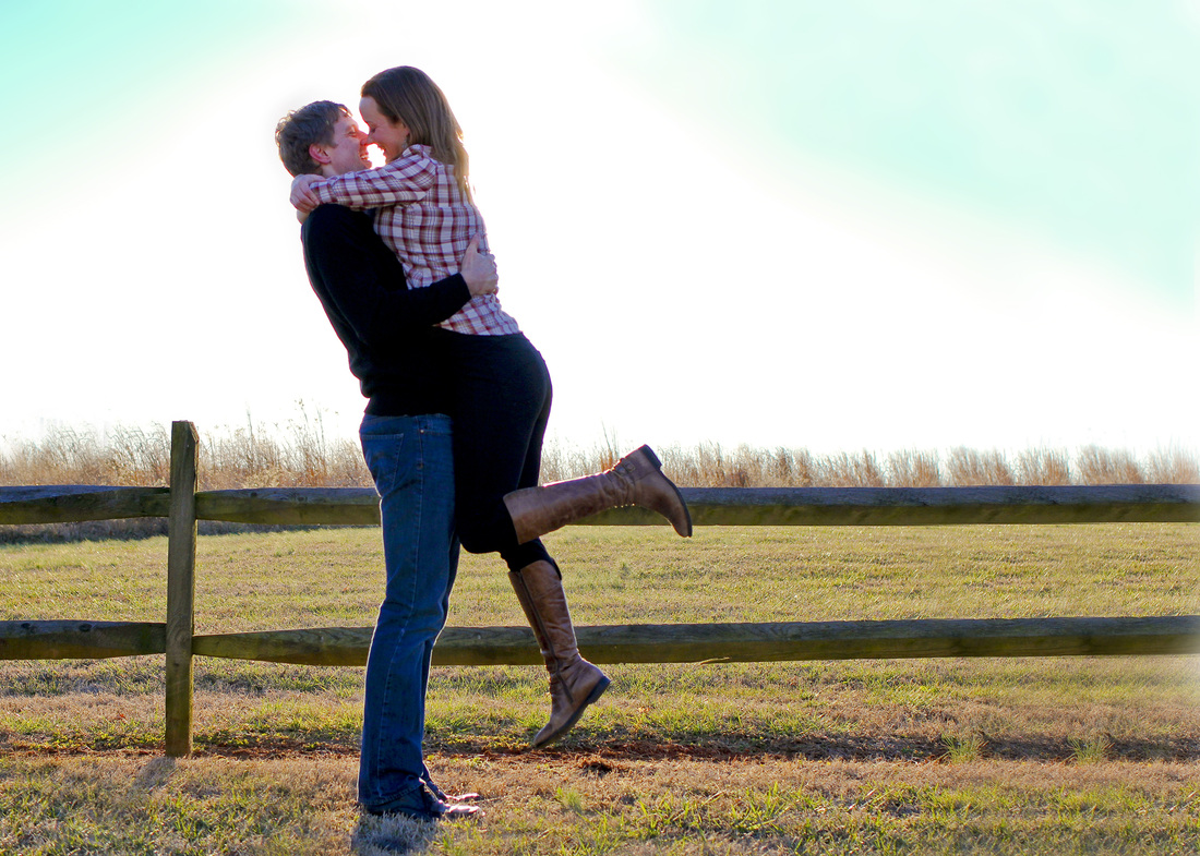 Portraits: Winter engagement photo session. Couple kissing in front of fence and tall grass. By Calm Cradle Photo & Design