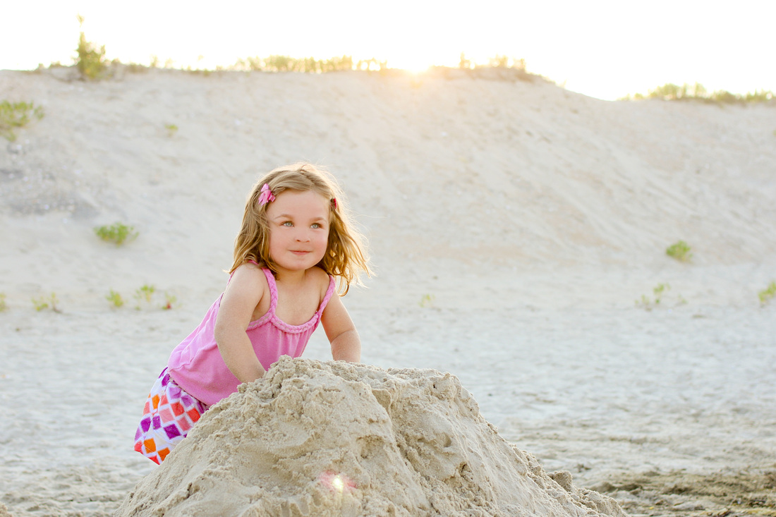 Portrait: Little girl climbing on a sandcastle in front of the dunes. Beach. By Calm Cradle Photo & Design